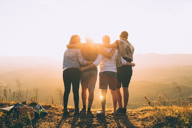 four people standing together and facing a sunset