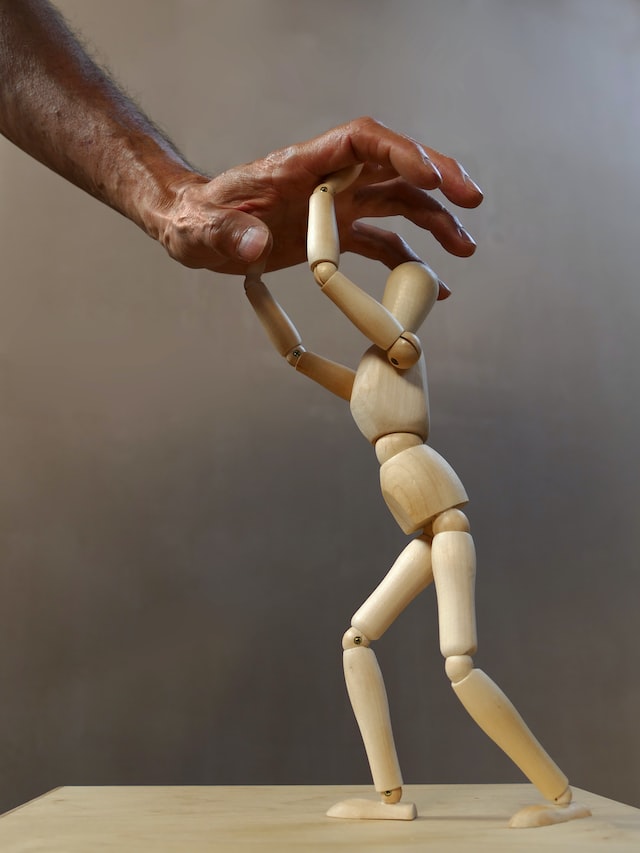 small, wooden, human-shaped figure pushing against a hand