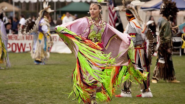 Native American woman in traditional dress dancing.