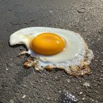 A fried egg sits on pavement, the yolk is mustard yellow color.