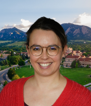 Laura Sochas is smiling and wears a bright red cardigan and tan, circular glasses.