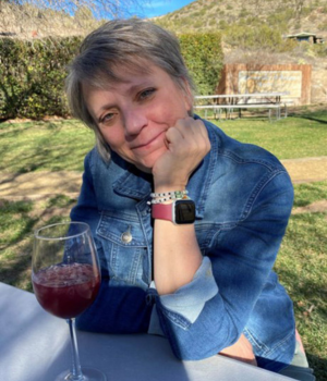 Denise Porchetta at picnic table with glass of wine, wearing a jean jacket.