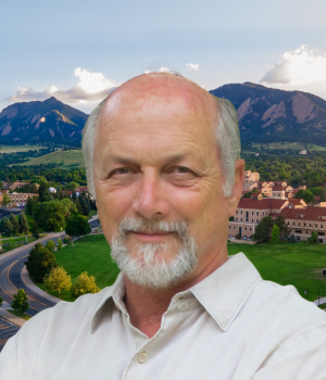 Gary Machlis wears a white collared shirt. A view of the Boulder Flatirons is in the background.