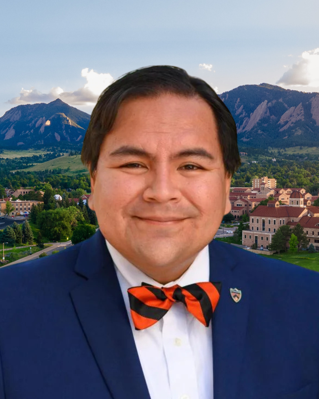 Michelangelo Landgrave wears a blue coat and orange and black bowtie. In the background, the CU Boulder campus with view of the Boulder Flatirons.