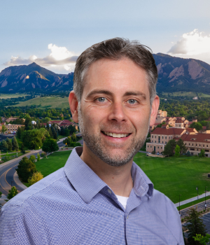 Shane Singh wears a blue collared shirt. In the background, the CU Boulder campus with the Flatirons.