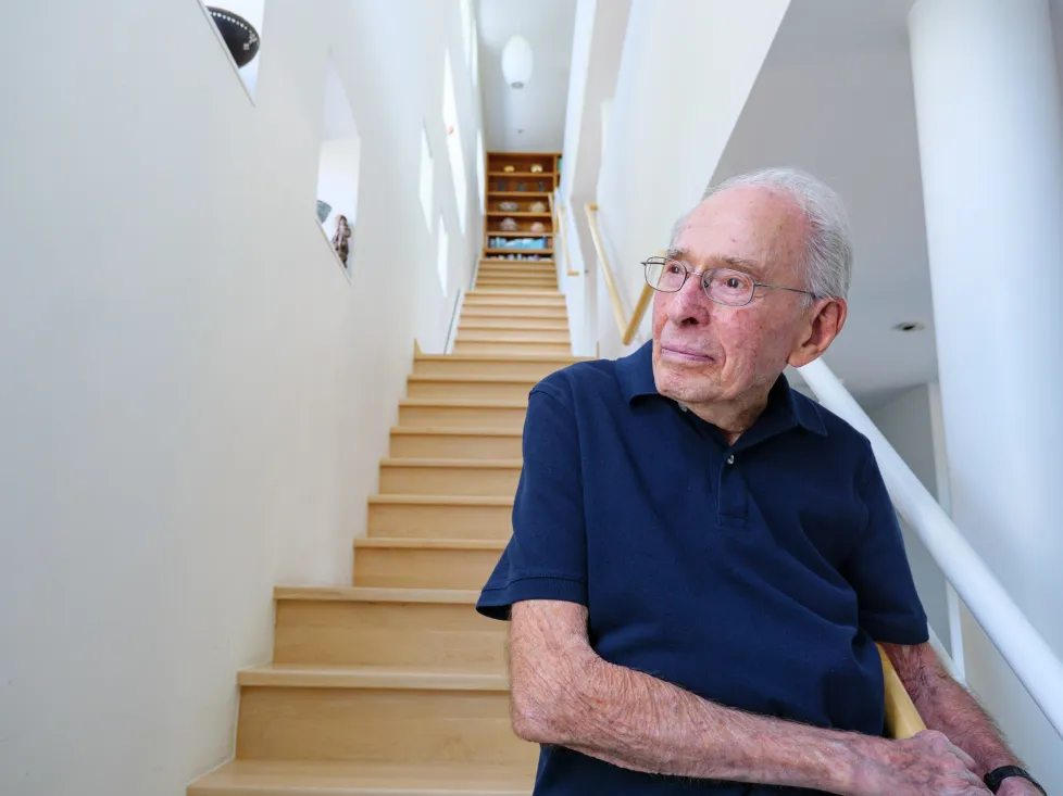 Richard Jessor wears a navy polo shirt and stands at the bottom of a stairwell.