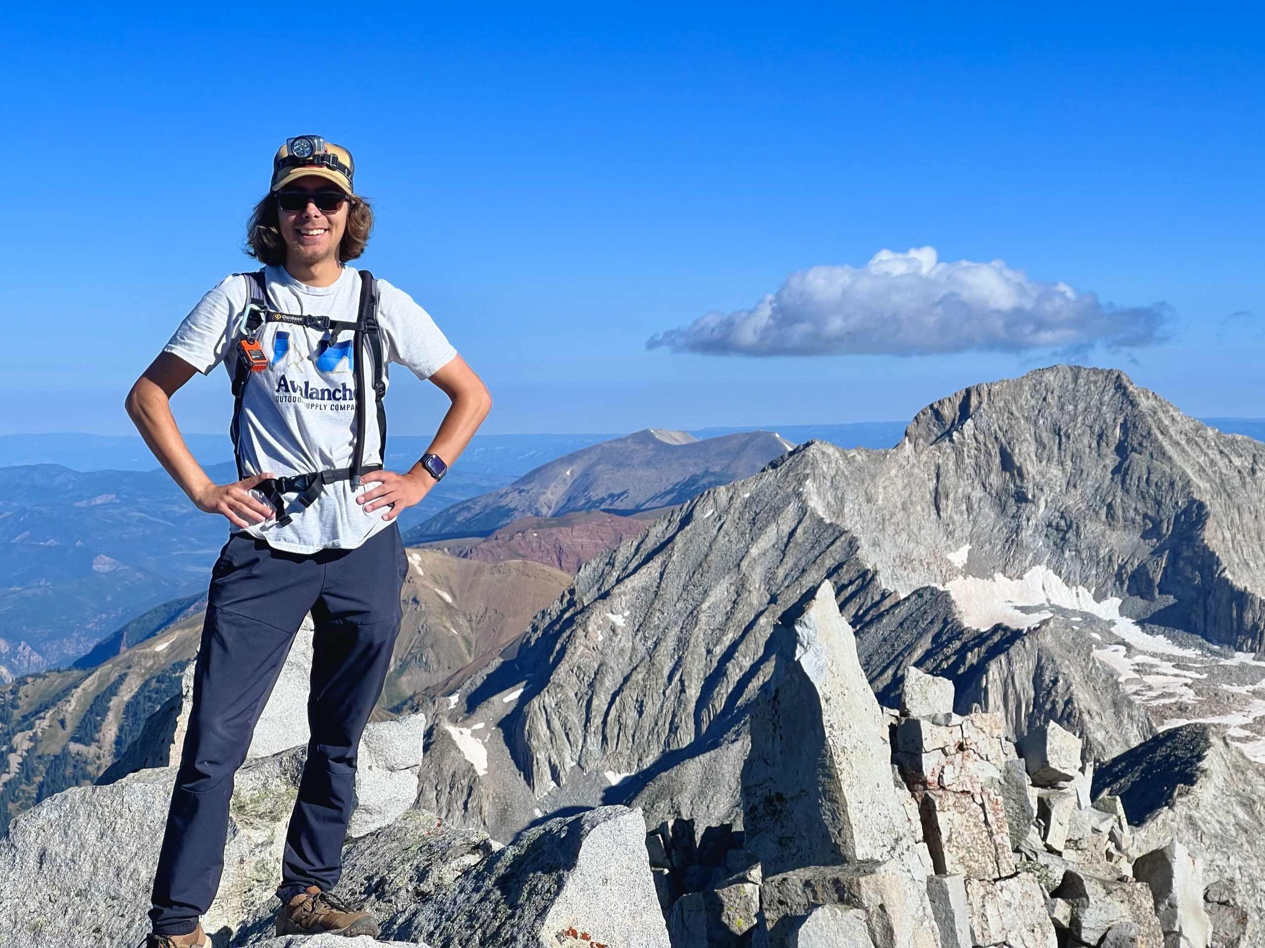 Lucas Gauthier at the top of a Colorado 14er. A view of the mountains are in the distance, the top is very rocky.