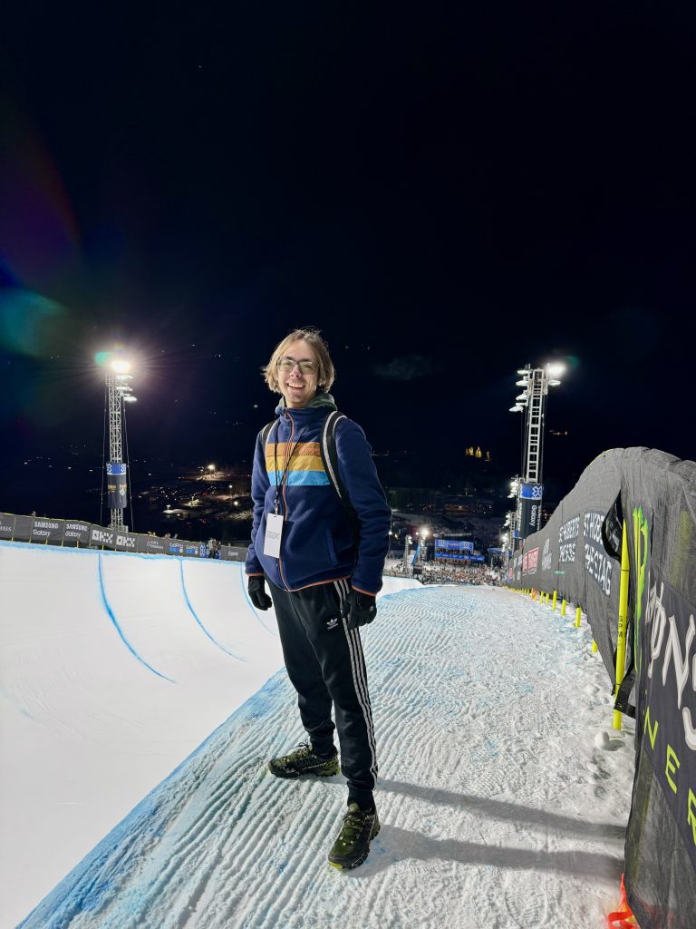 Lucas at a skiing terrain park at night. He wears a pass on a lanyard.