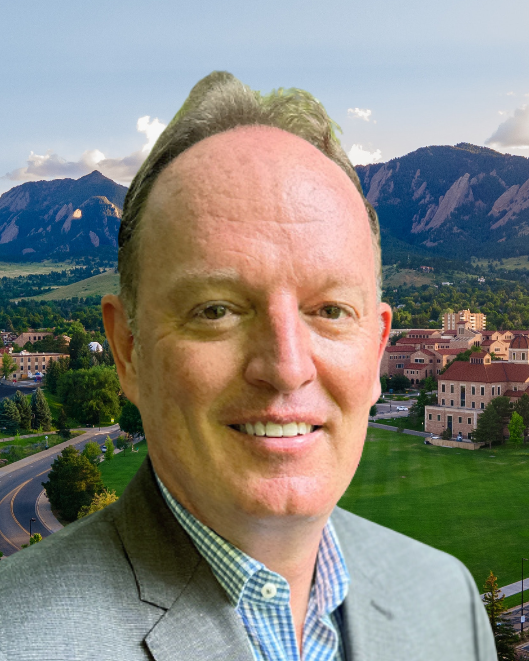 Brian King wears a grey suit. Behind him, a view of the Boulder Flatirons and CU Boulder campus.