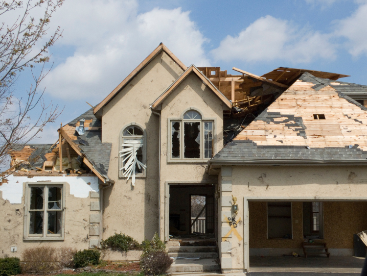 A home in a typical neighborhood suffers from fire damage, with broken windows and a crumbling roof.