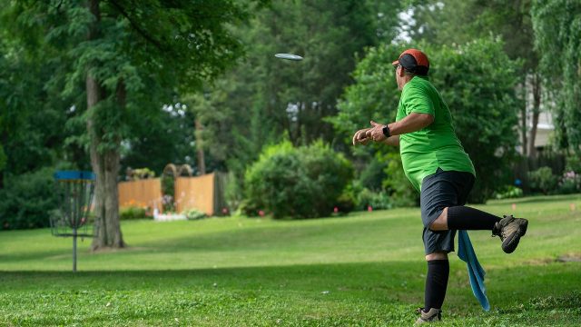 A man throws a frisbee into a disc golf goal at a lush, green park.