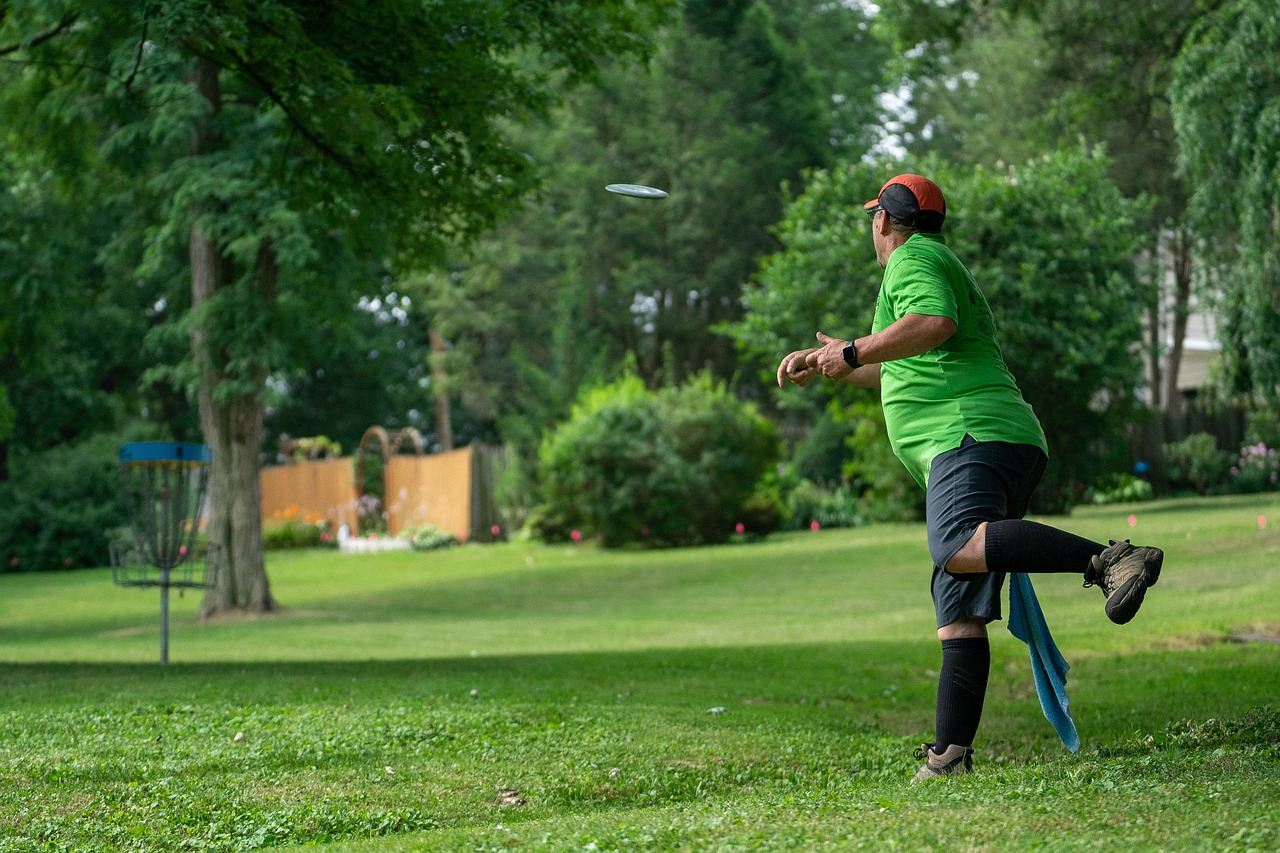 A man throws a frisbee into a disc golf goal at a lush, green park.