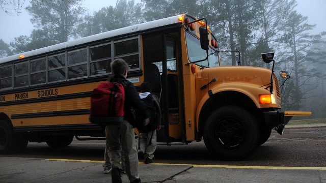 Three students wait to board a school bus on a foggy morning.