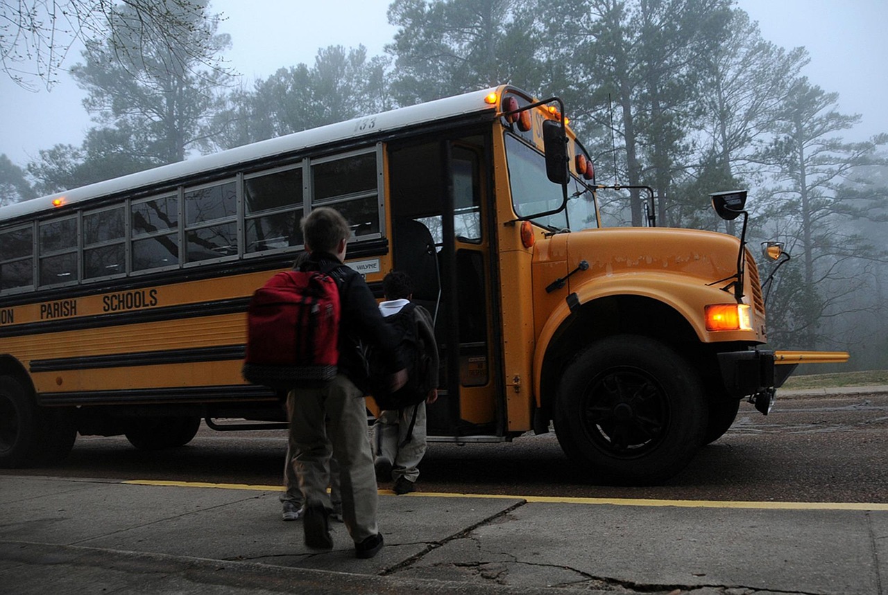 Three students wait to board a school bus on a foggy morning.